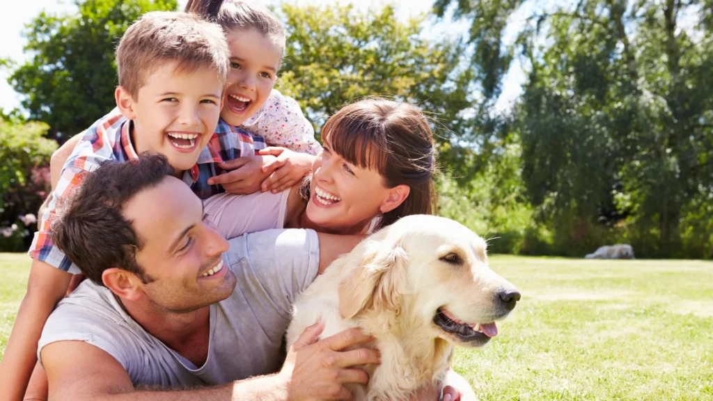 Happy family with two kids and a golden retriever playing together on the grass in a sunny park.